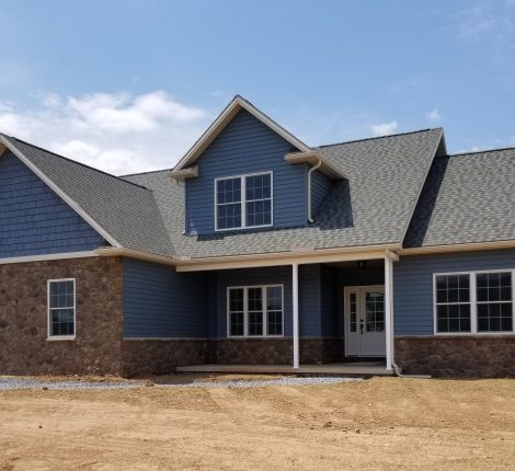 Deer Ridge Construction new home with 2 stories, blue siding, stone accents, a covered front porch, and a gray asphalt roof.