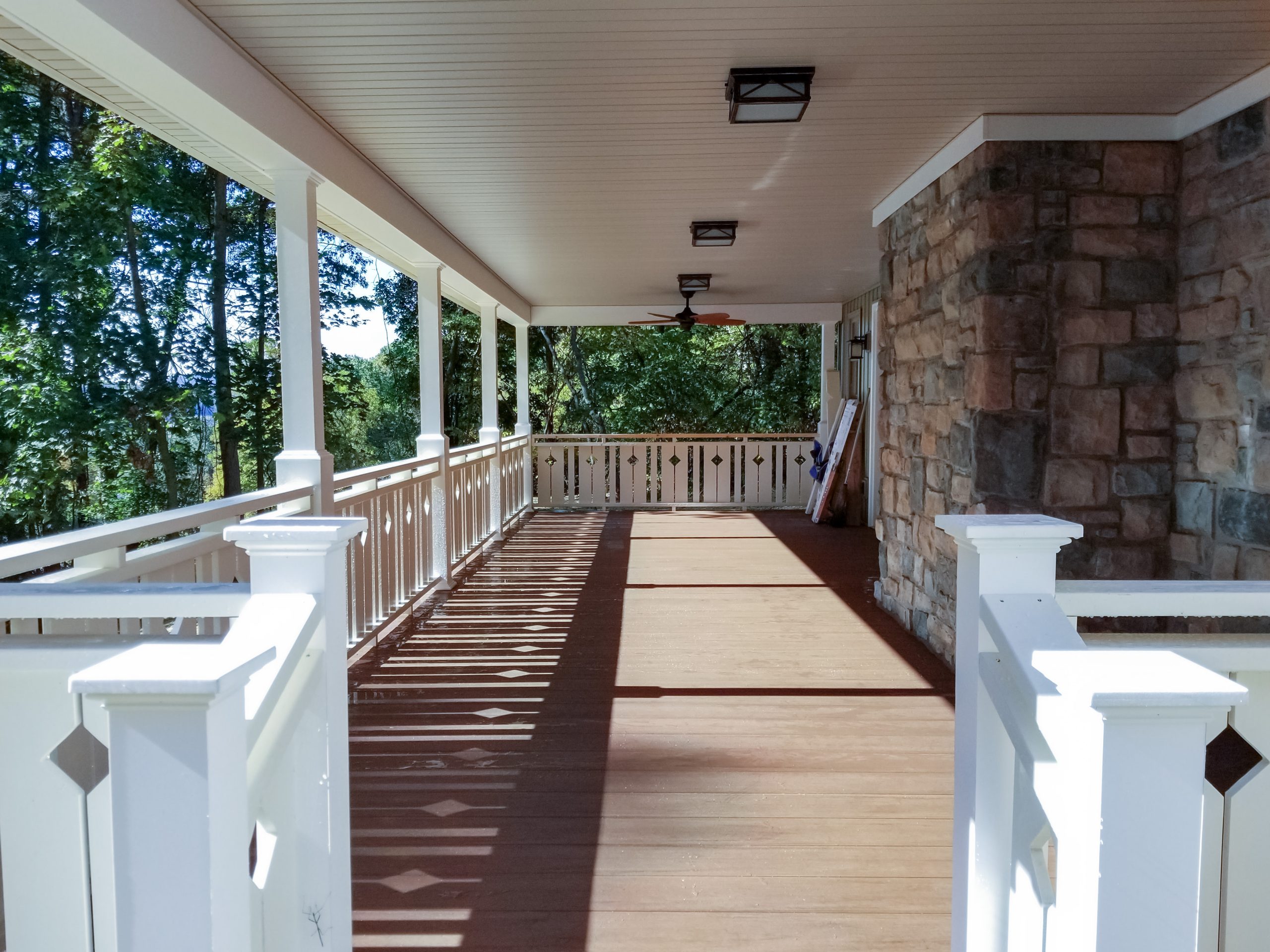 Front porch and deck covered with a ceiling and surrounded with white vinyl railings.