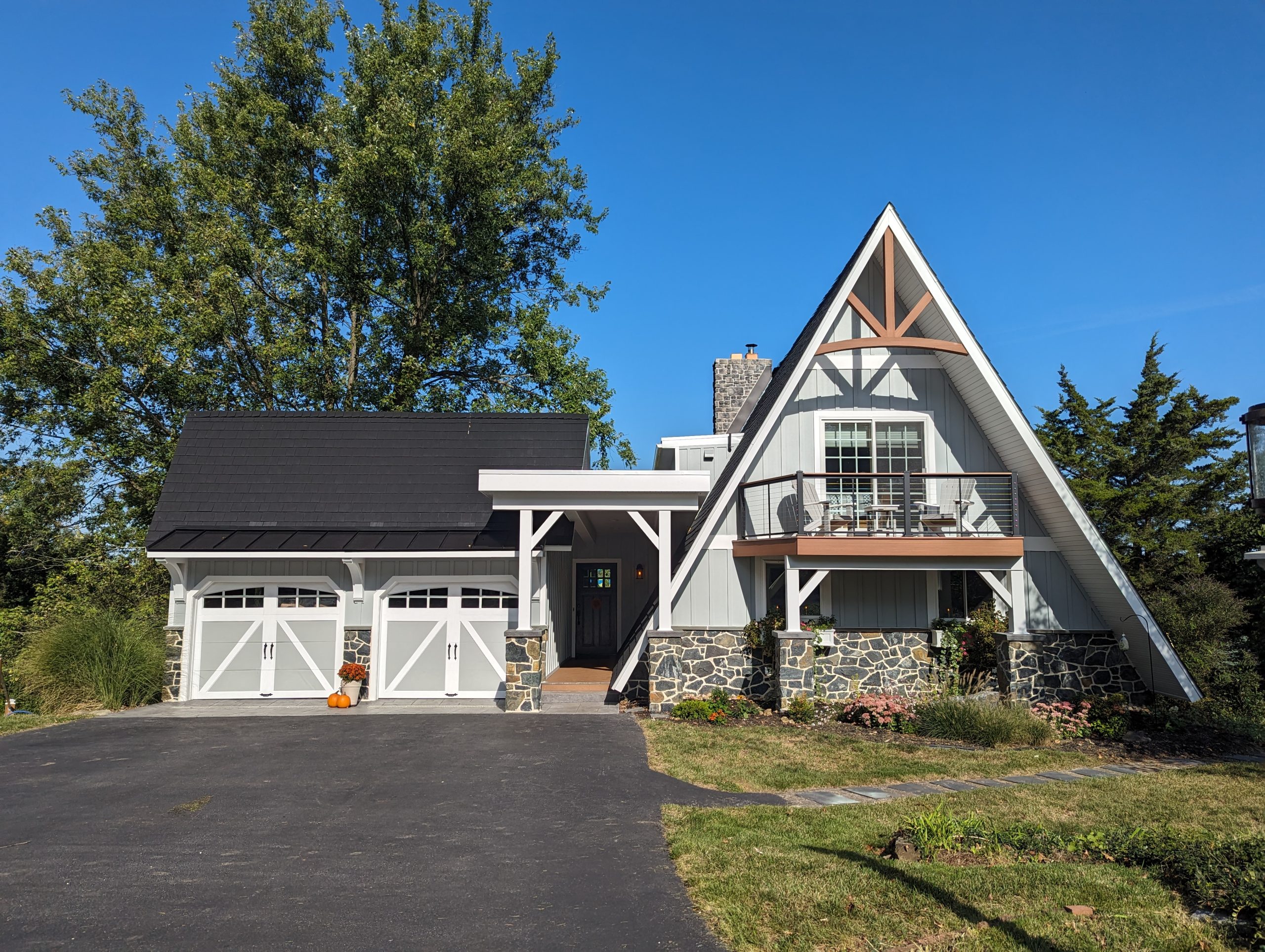 Front exterior of a unique triangle shaped home with new light gray siding, white trim, stone accents, brown balcony, and a matching 2-car garage