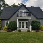 Front exterior view of a remodeled home with gray siding, gray stone accents, black roofing, and a balcony over the home entrance.