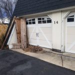 Close up of the exterior of a 2 car garage with light yellow siding, white trim, and black roofing.