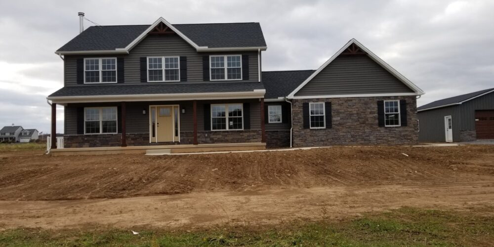 Front exterior view of a new home with dark gray siding, black shutters, stone siding, white trim, an attached garage, and black roofing.