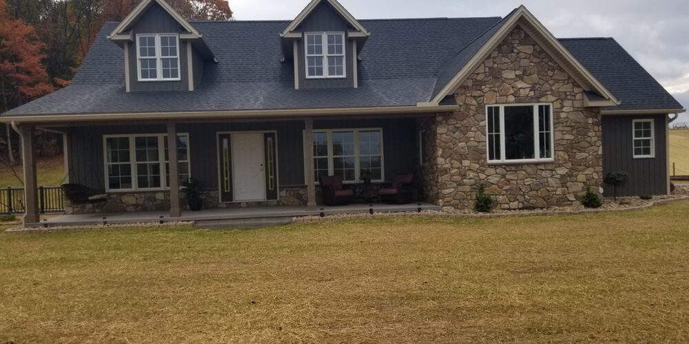 Front exterior view of a new home with dark gray siding, black roofing, stone accents, and a covered front porch.