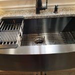 Close up of a stainless steel kitchen sink with speckled granite countertops, a black kitchen faucet, and a utensil drainer holder in the sink.