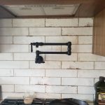 Close up of a black adjustable water faucet for filling pots that is attached to the kitchen wall and above the stove.
