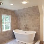 Close up of a shower and tub combination with a white soaking tub, gray tiled walls, and gray tiled shower flooring in a remodeled bathroom.