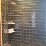 Close up of a tile shower and tub combination with dark gray subway tile walls and a white tub base.