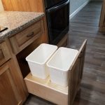 Close up of a kitchen cabinet opened with 2 white trash bins inside.