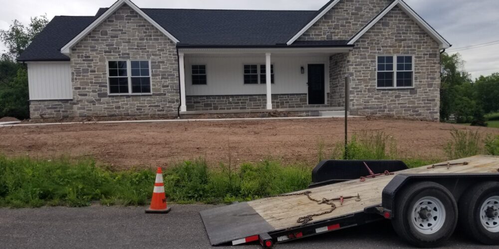 Front view of a new ranch home with stone veneer siding, white vertical shiplap siding, a covered front porch, and black roofing.