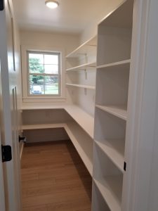 Empty pantry with white shelves, white walls, a window, and plank flooring.