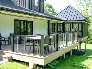 Deck with wicker outdoor furniture on a home with white walls and black roofing.