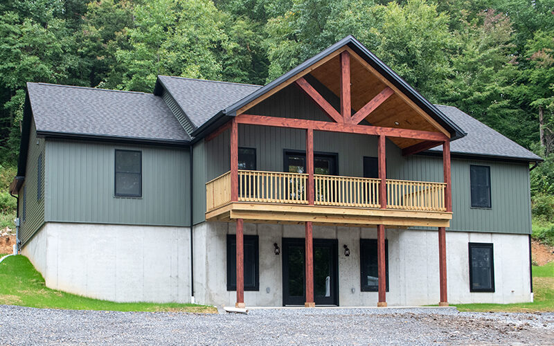 Front exterior view of a 2-story home with a white first story, green second story, black windows, black doors, black asphalt roofing, and a second story covered wood deck.