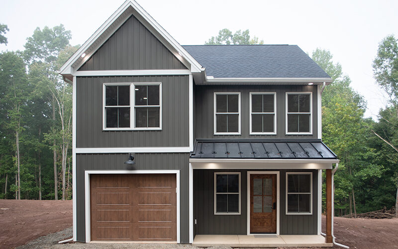 Front exterior view of a 2-story home with dark gray siding, white trim, a brown garage door, a covered front porch, and a brown front door.