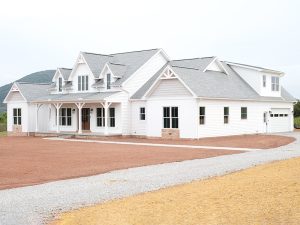Front and right side exterior of a home with white siding, gray asphalt roofing, brick veneer, decorative shakes, a covered front porch, a white garage door with windows, and a white single-entry side door.