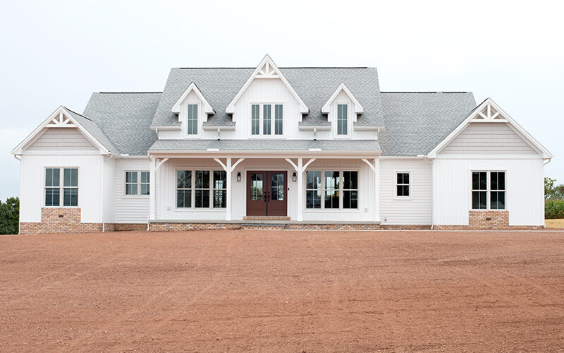 Front exterior of a home with white siding, gray asphalt roofing, brick veneer, decorative shakes, a covered front porch, and brown double doors.