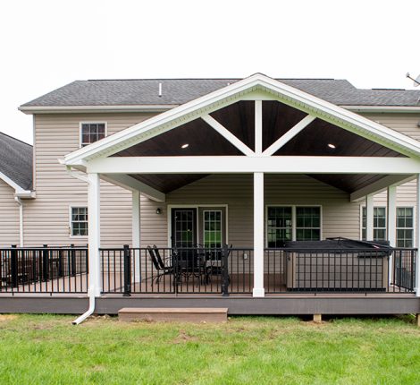 New covered deck with brown decking, white beams and posts, black aluminum railings, a black outdoor dining set, a hot tub, and a brown plank ceiling with puck lights.