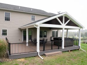 New covered deck with brown decking, white beams and posts, black aluminum railings, a black outdoor dining set, a hot tub, and a brown plank ceiling with puck lights.