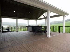 New covered deck with brown flooring, white beams and posts, black aluminum railings, a black outdoor dining set, a hot tub, and a brown plank ceiling with puck lights.