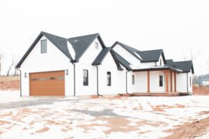 side view of new home with white siding, patio with wooden beams, gray roof, and wooden garage door with windows