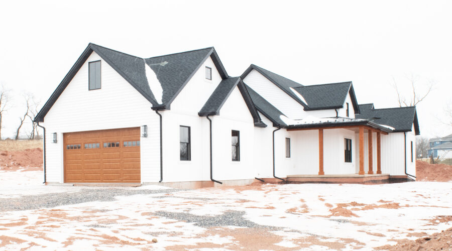 side view of new home with white siding, patio with wooden beams, gray roof, and wooden garage door with windows