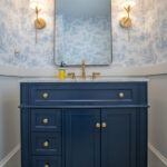 remodeled bathroom with blue sink, gold fixtures, square mirror, and blue floral wallpaper