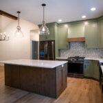 kitchen in a new home with green cabinets, white countertops, wooden island, and black appliances