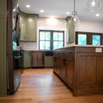 close up of a new kitchen with wooden floor and island, green cabinets, and black appliances