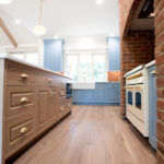 new kitchen with hardwood floors, island, blue cabinets, and brick arch around stove
