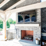 stone fireplace with a TV on a back porch