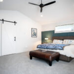 renovated bedroom with a sliding barn door, green paneling, and ceiling fan