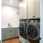 laundry room with new appliances and sink with green cabinets