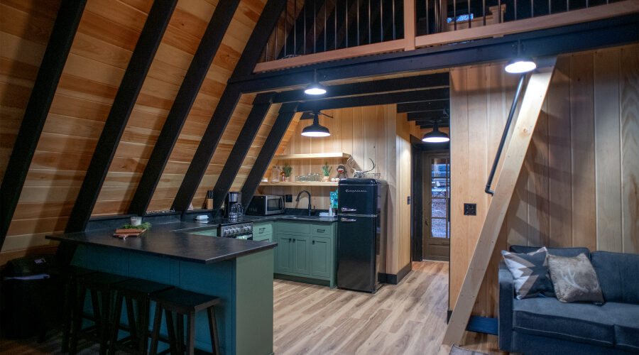new remodeled kitchen with green cabinets, black appliances, and hardwood walls