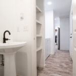 bathroom with pedestal sink, shelves, leading to a laundry room