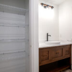 large sink with hardwood cabinets and white countertop next to closet space with shelves