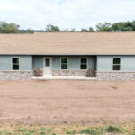 front view of new home with a front porch, green siding, and stone veneer